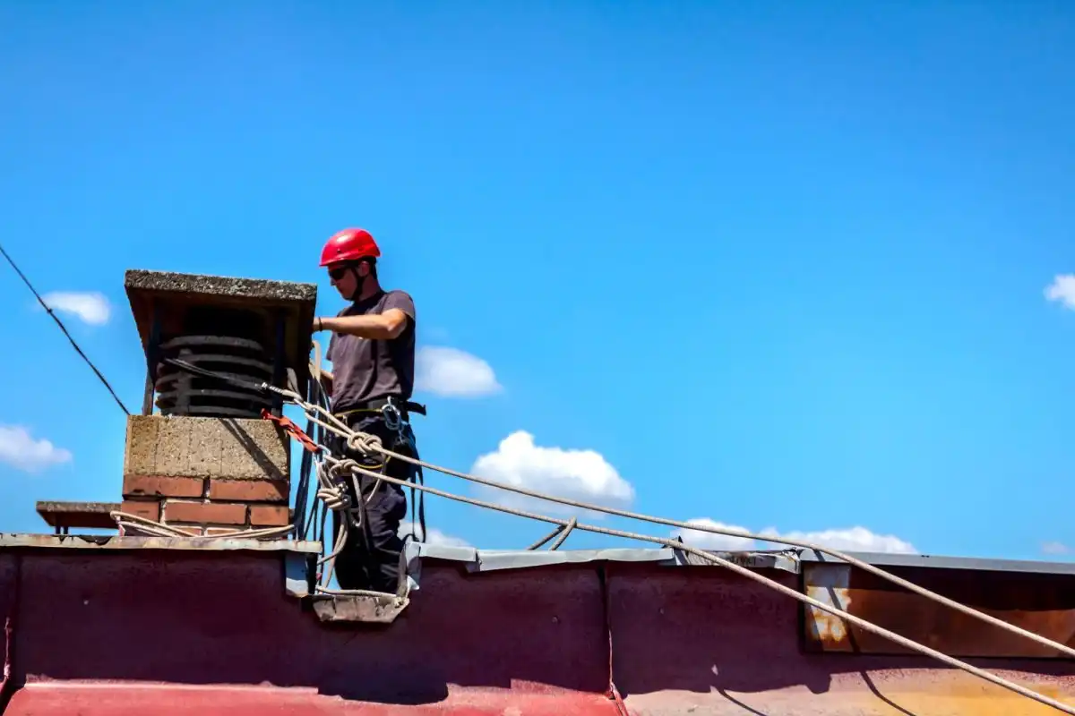 Worker tied off with a rope on a roof, next to a chimney